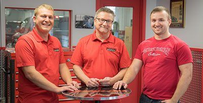 Three men in red shirts are standing next to each other in a garage.