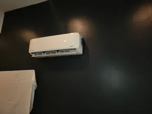 White wall-mounted air conditioner on a dark green wall, with part of a beige sofa visible below.