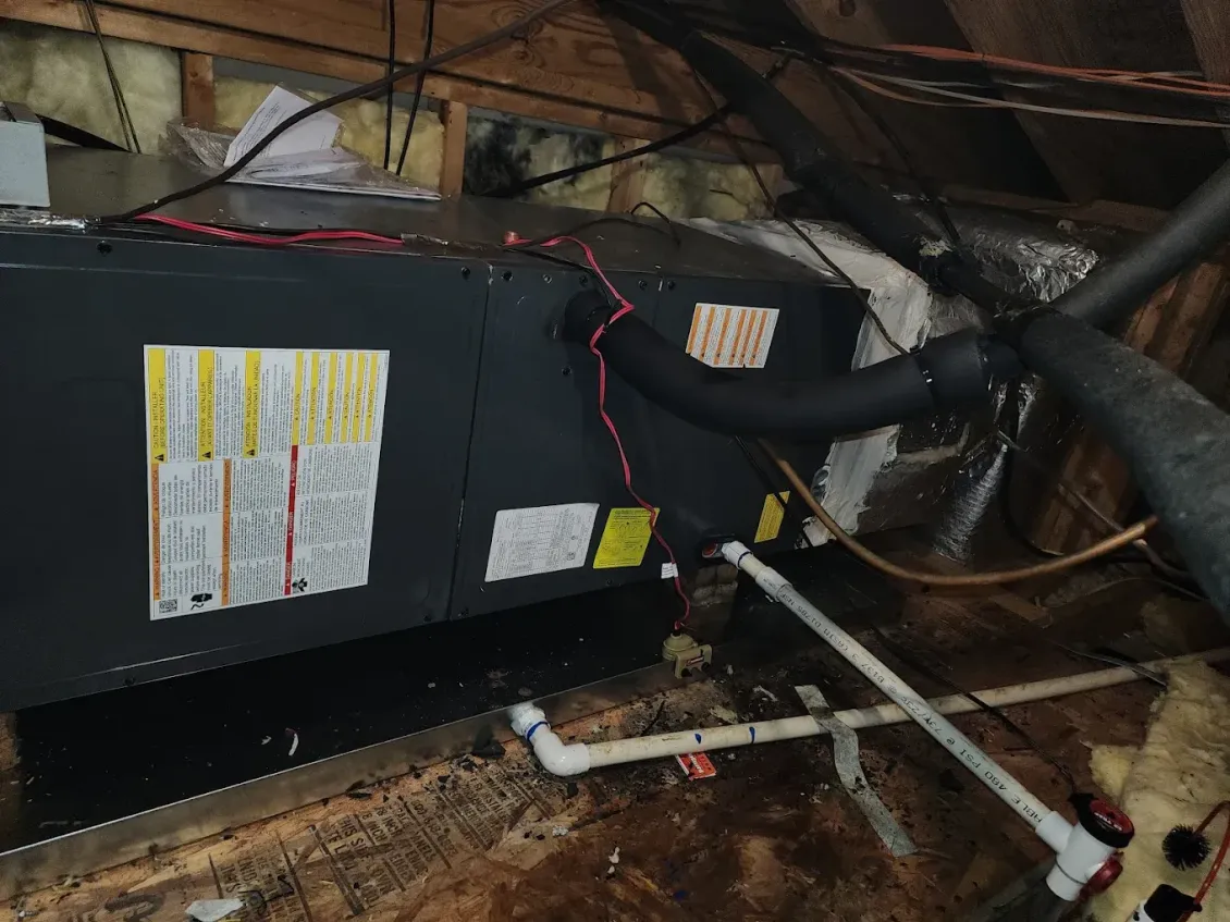 Black HVAC unit in a crawlspace with exposed pipes and ducts.