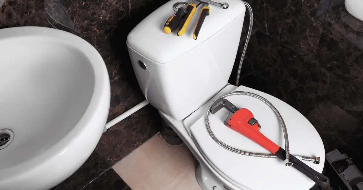 Toilet with plumbing tools laid out, near a sink.