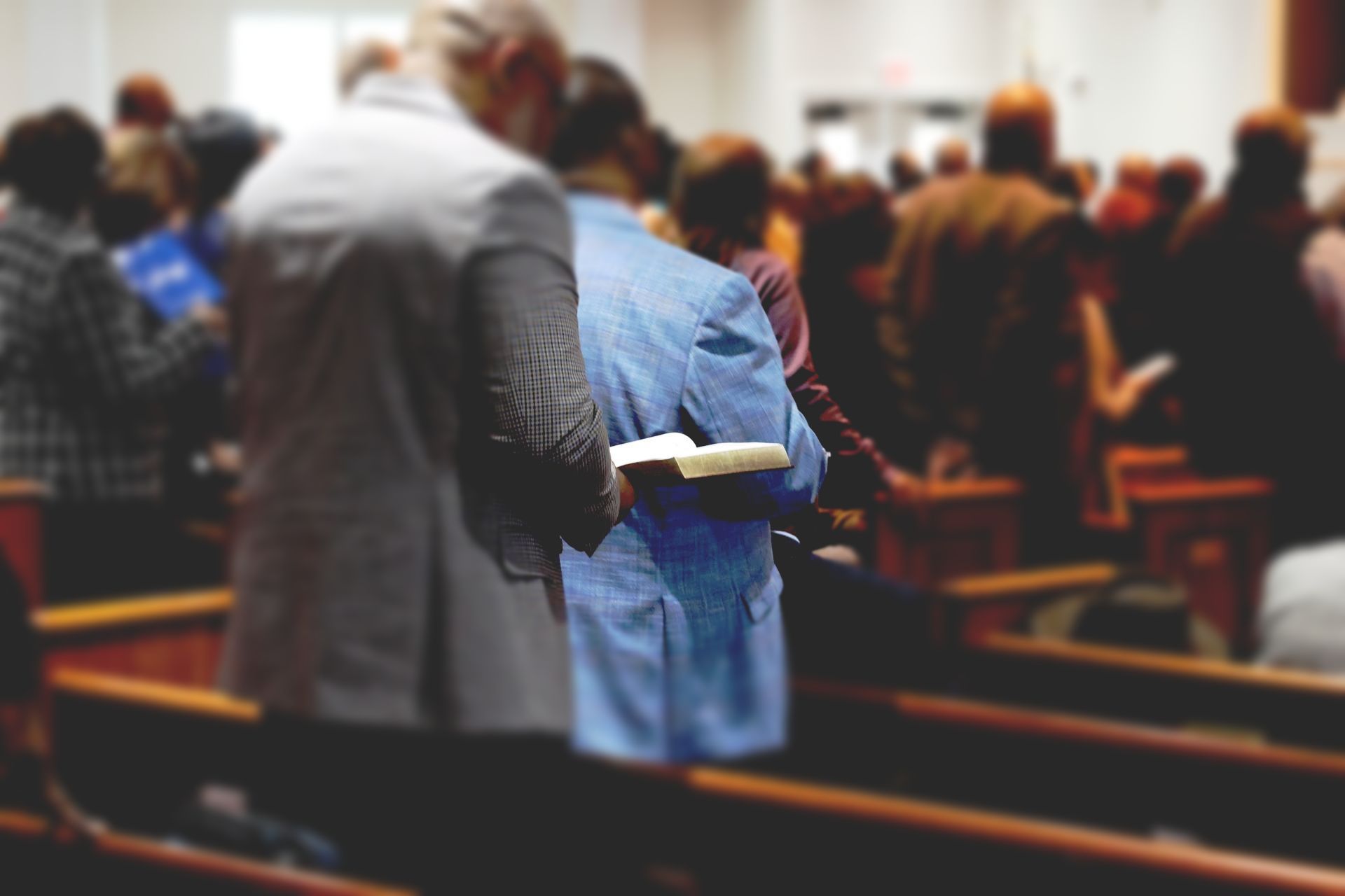 People stand in rows of wooden pews in a church, holding open books while participating in a service.