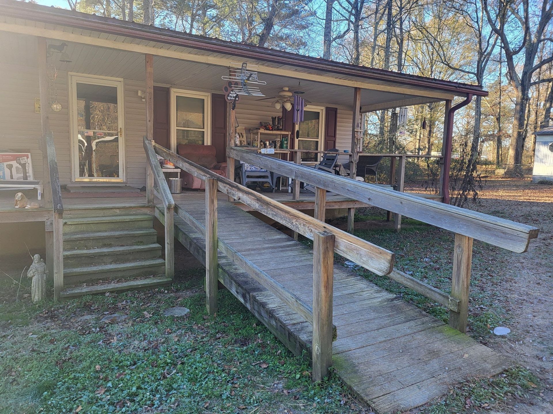 House porch with central stairs and wheelchair ramp, with handrails and wooden walkway in a wooded yard.