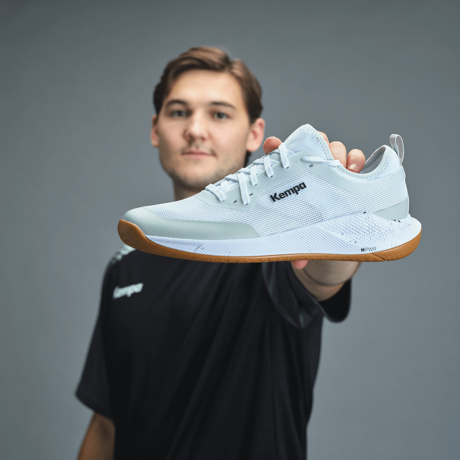 Maður heldur á ljósbláum Kempa handboltaskó.