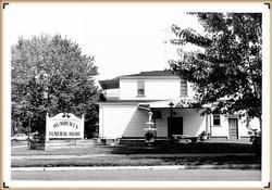 Black-and-white photo of a house beside a sign reading “... Funeral Home”
