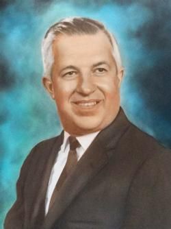 Formal studio portrait of a smiling man in a dark suit and tie against a blue background