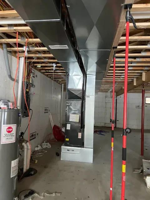 Basement with HVAC system, water heater, and supporting jacks. Gray ductwork, concrete floor, unfinished walls.
