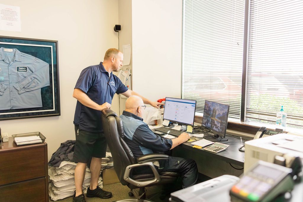 Two men at desk, one pointing at computer screen, other seated in office | Stephen's Automotive