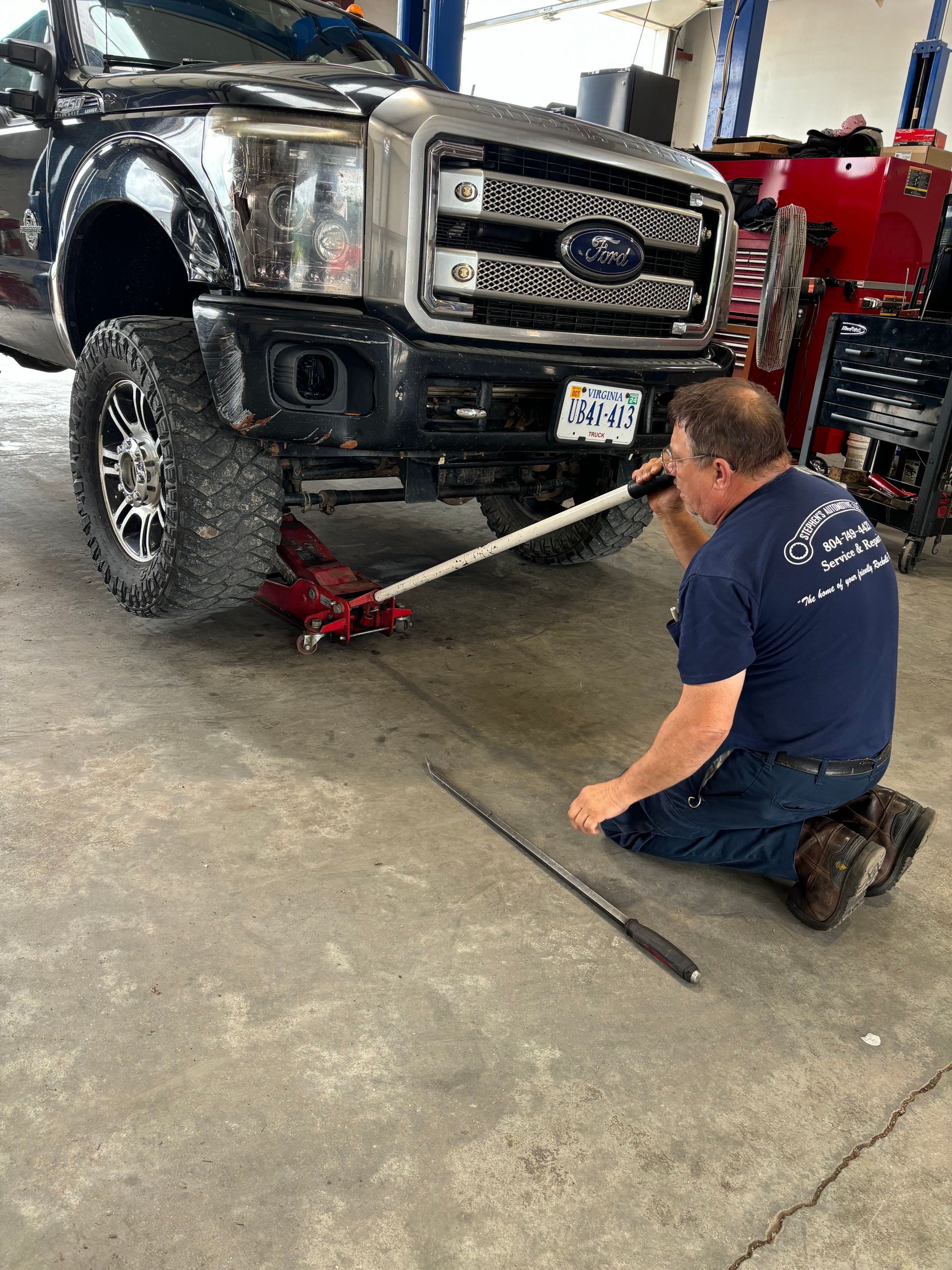 Mechanic kneeling, using a jack to lift a black truck | Stephen's Automotive