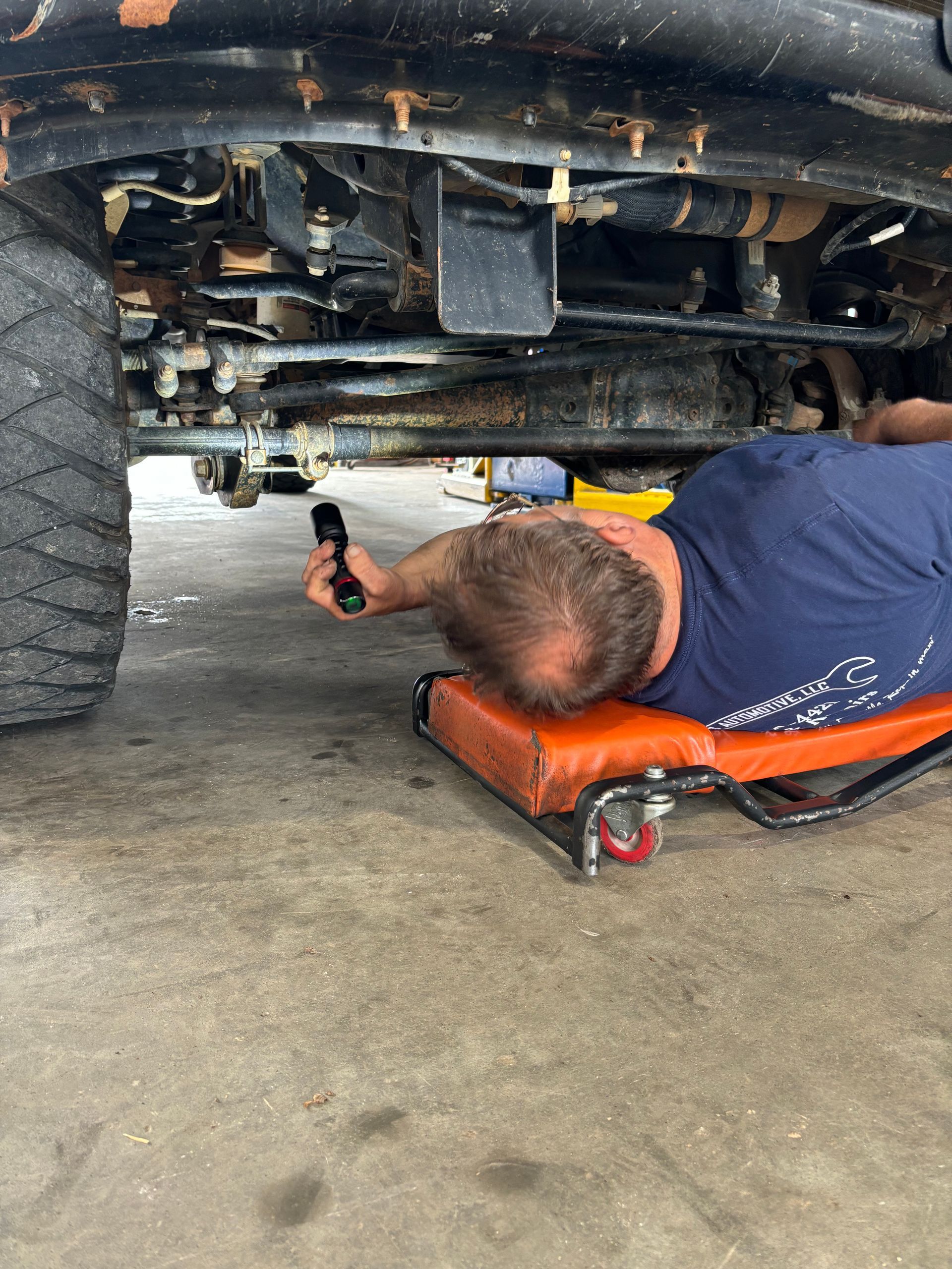 Mechanic on a creeper inspecting the underside of a vehicle with a flashlight | Stephen's Automotive