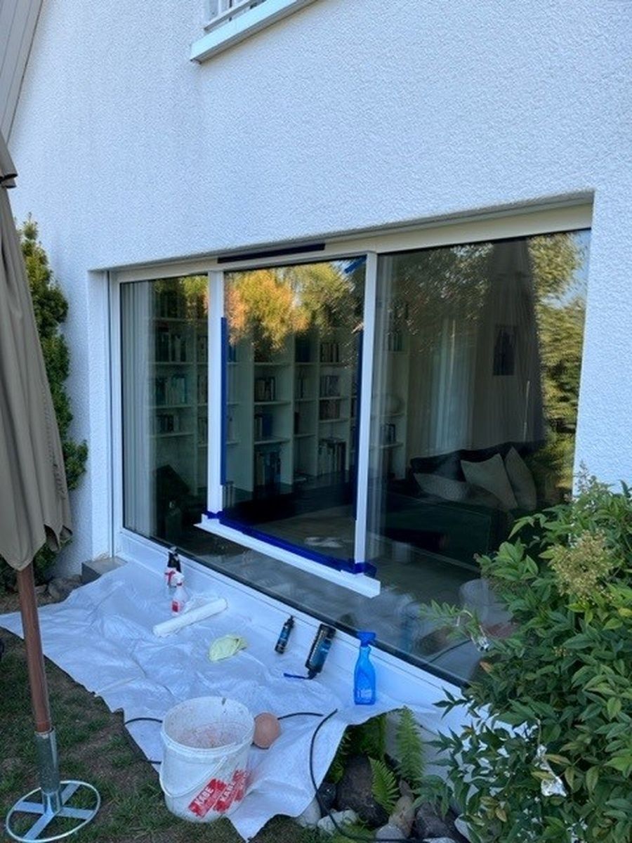 An der Aussenseite eines Hauses wird ein Fenster gestrichen.