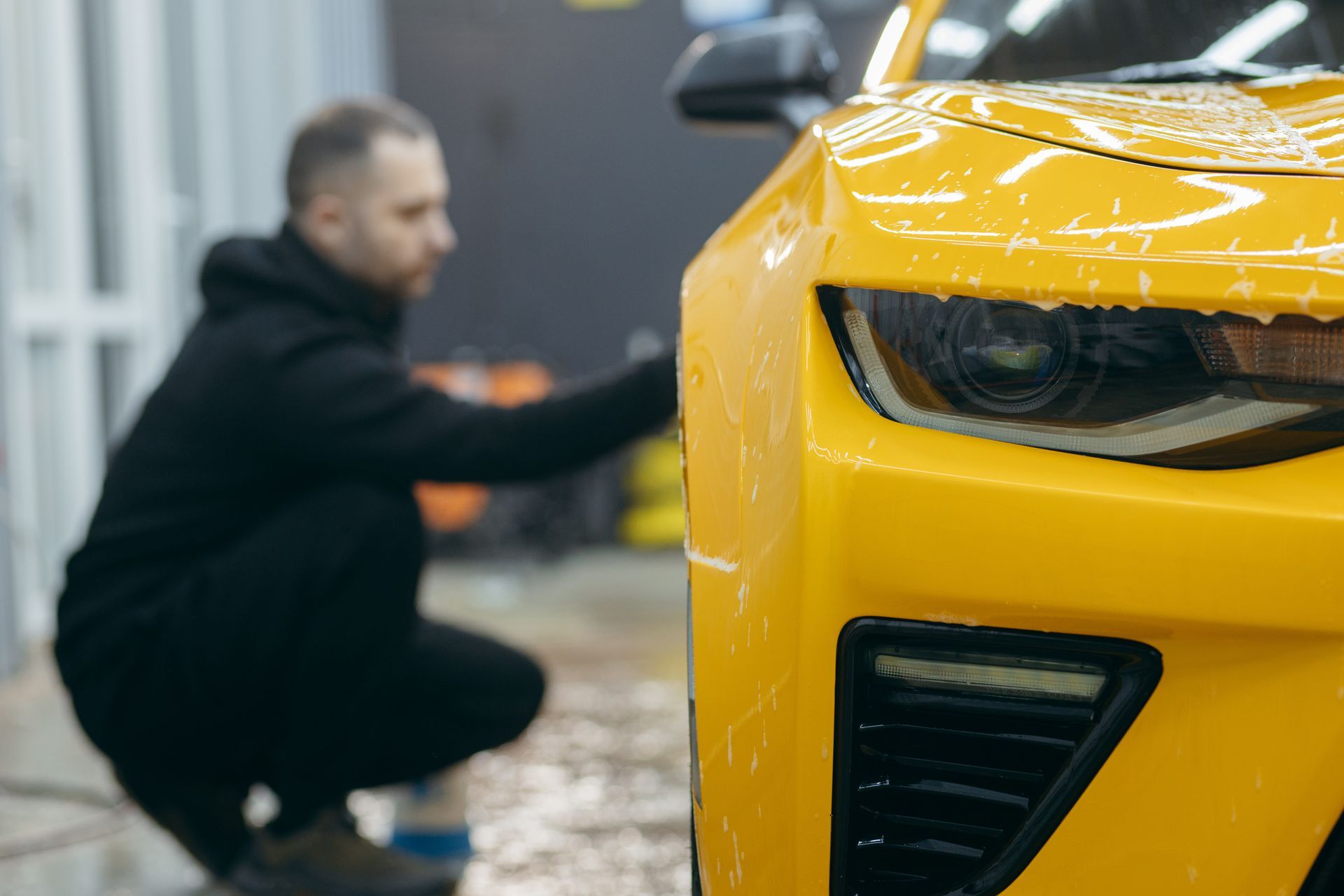 A man washes the side of a yellow car, using a small water spray after a detail. A man washes the side of a yellow car, using a small water spray after a detail.