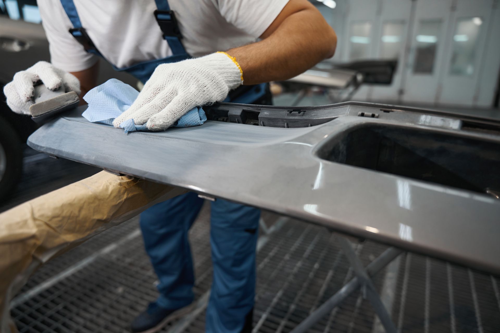 A close-up of a specialist is cleaning car parts before painting in a garage.