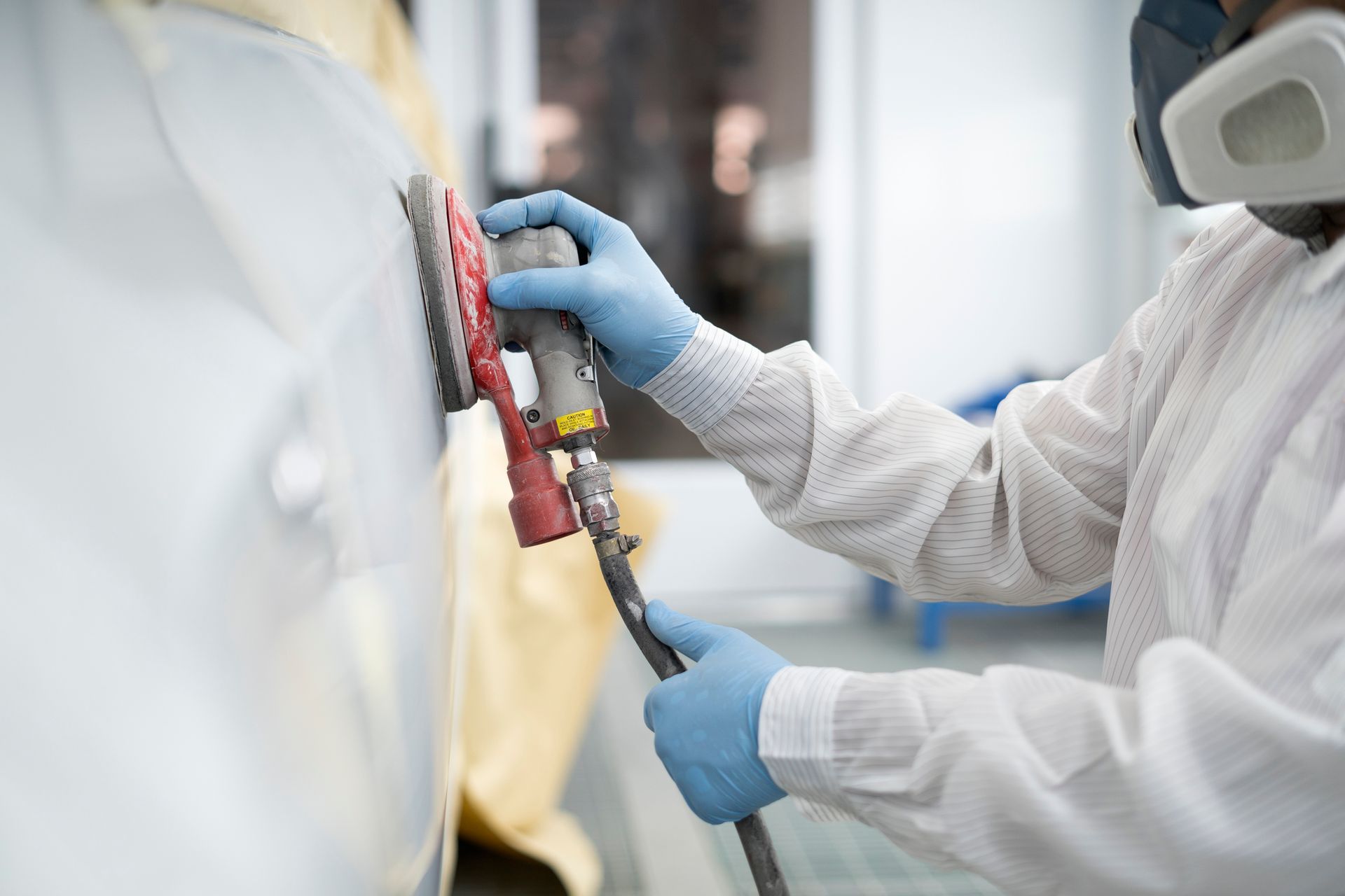 Worker uses electric polisher to wax white car door during collision repair in auto shop garage.
