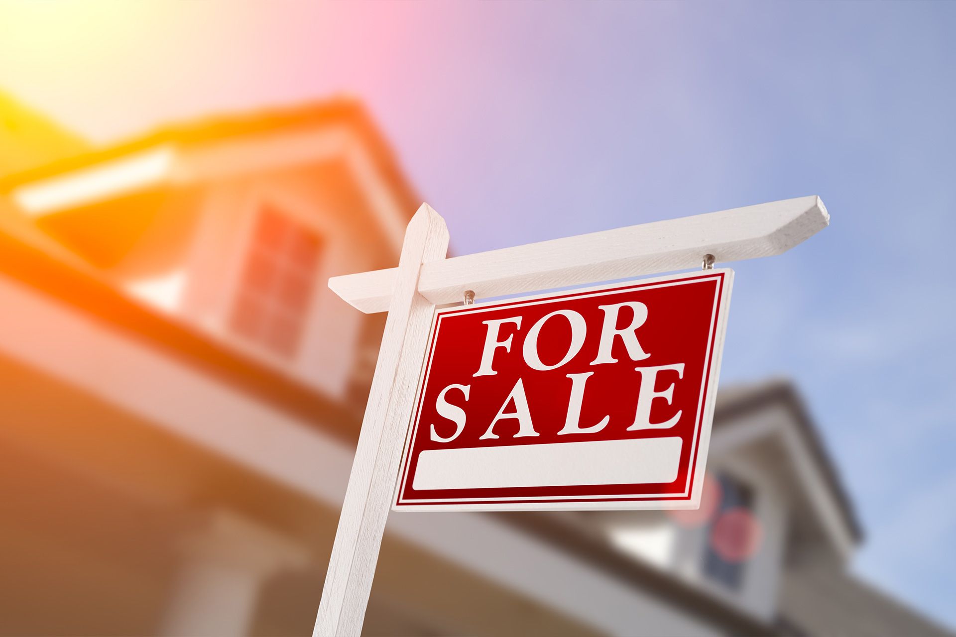 For sale sign in front of a blurred house with warm sunlight