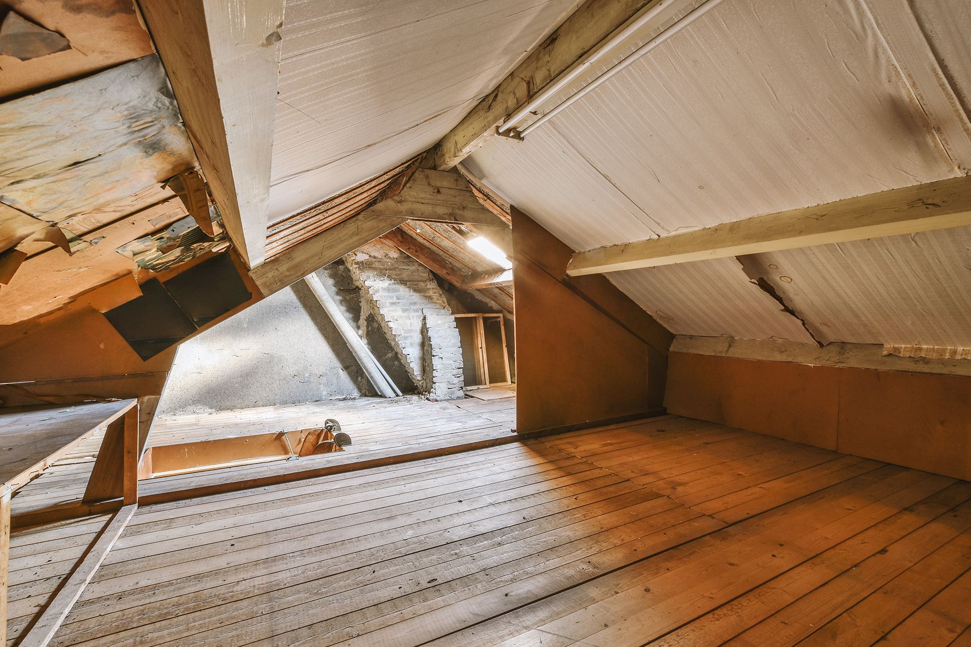 Dusty attic with exposed wooden beams and a small window letting in daylight