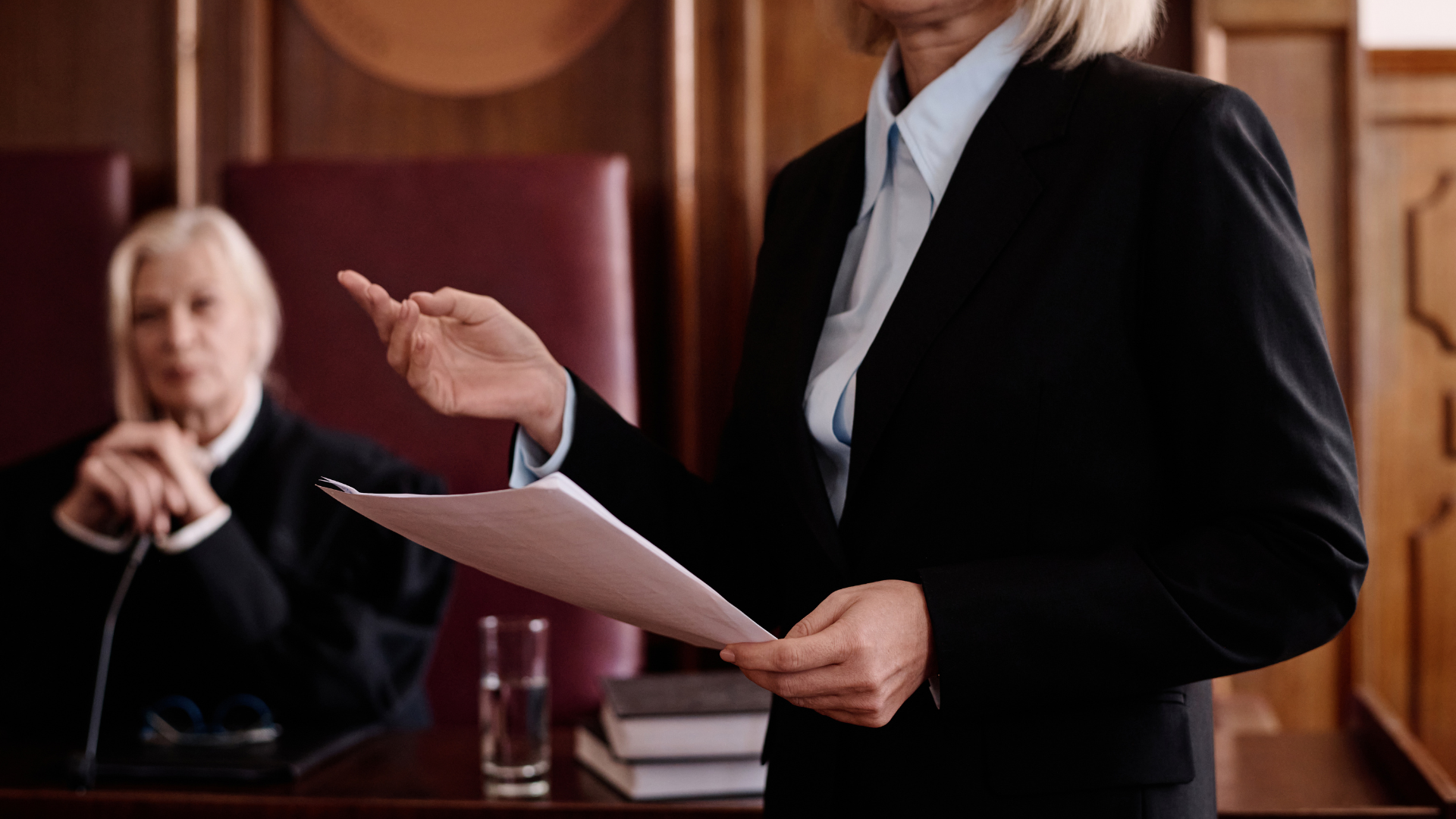 A woman is holding a piece of paper in front of a judge in a courtroom.