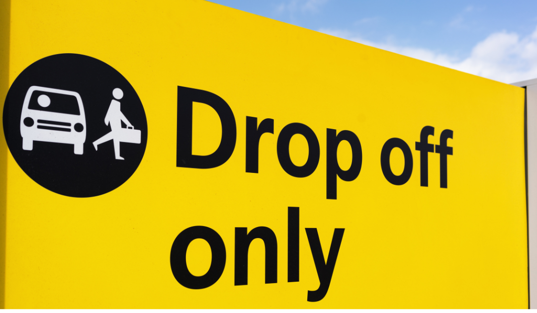 Airport yellow sign with a black circle showing a car and person. Text reads