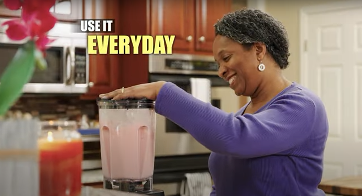 A woman is making a smoothie in a blender in a kitchen.