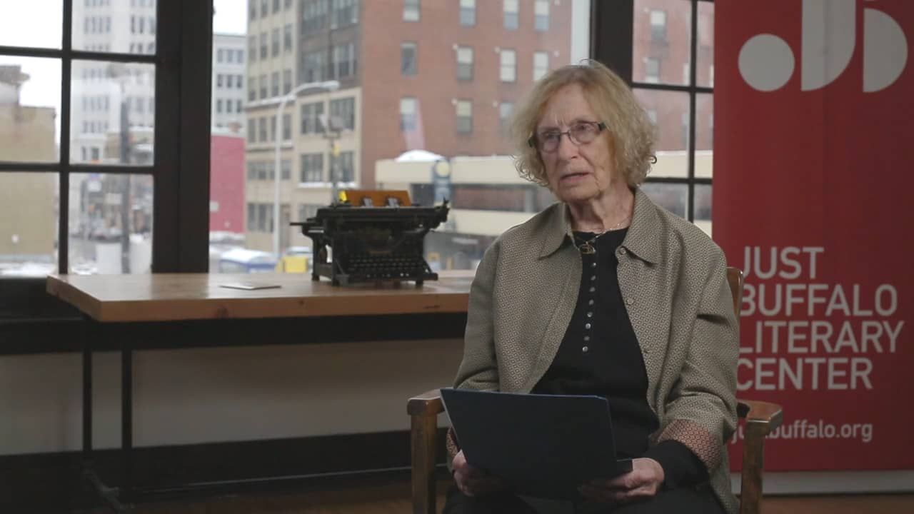 A woman is sitting in front of a sign that says just buffalo literary center