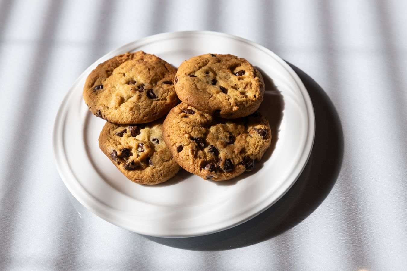 Four chocolate chip cookies are on a white plate