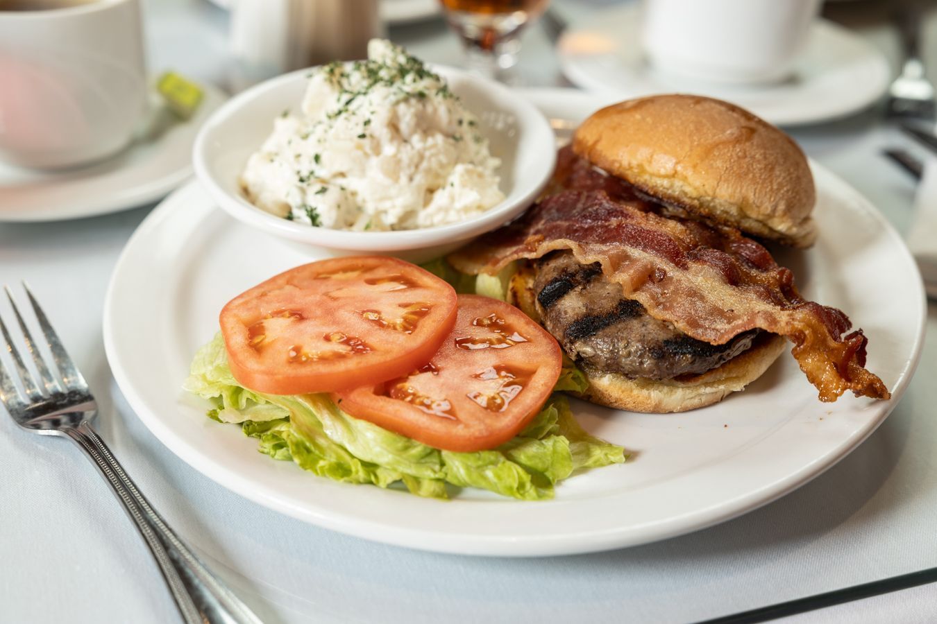 A white plate topped with a hamburger , bacon , lettuce and tomatoes.