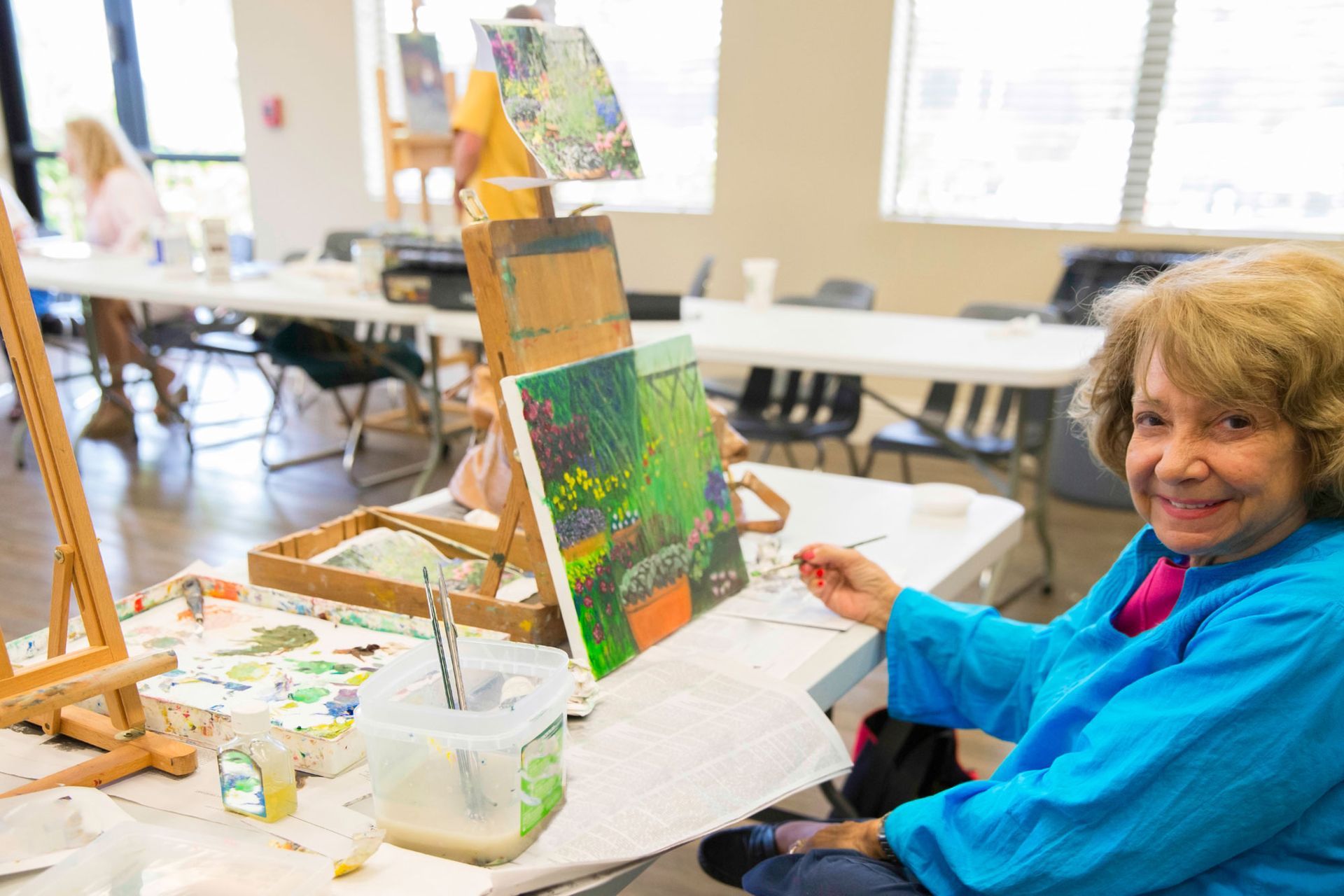 A woman is sitting at a table painting on an easel.