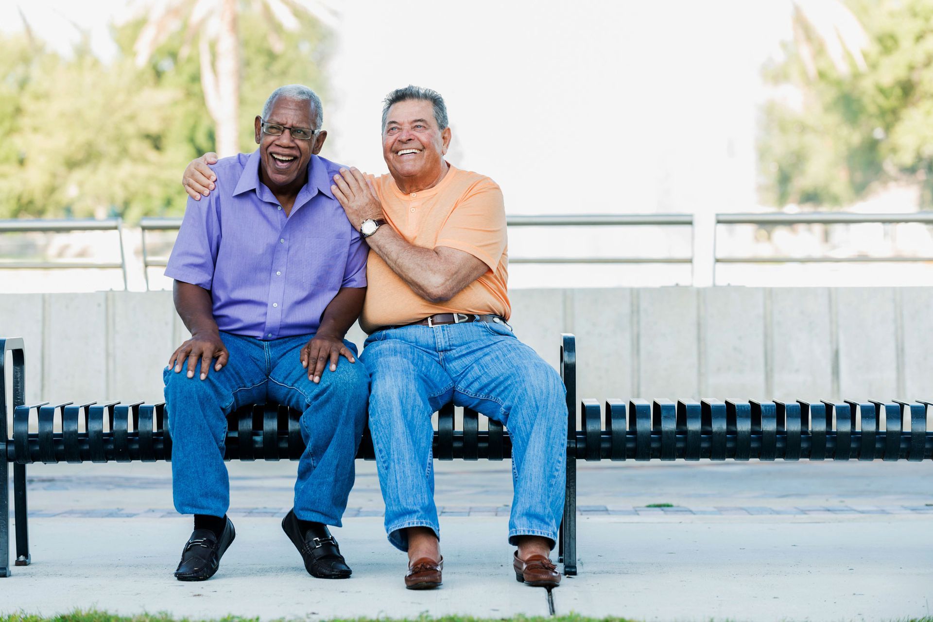 Two men are sitting on a bench with their arms around each other.