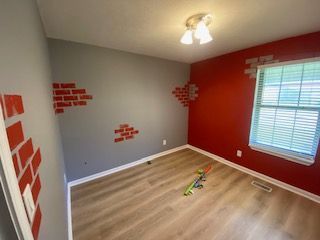 Room with gray and red walls, faux brick design, light wood floor, and window.
