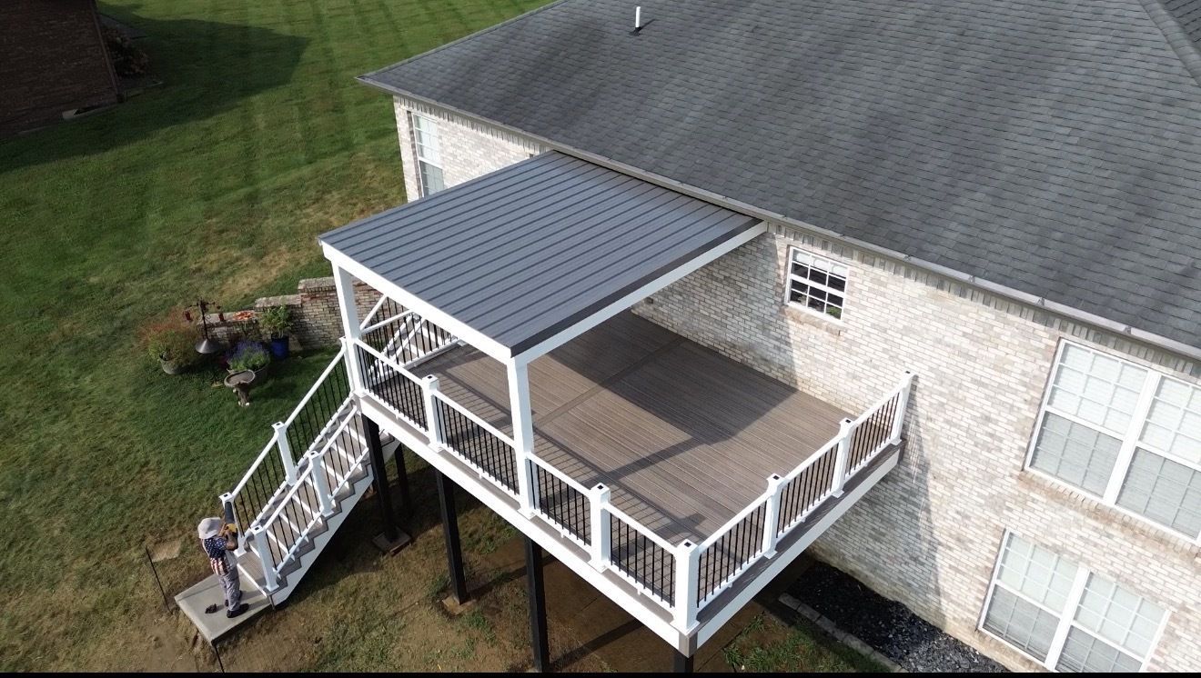 Wooden deck attached to a light-colored house with a sliding door and a small bush. Green grass in the foreground.