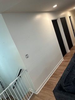 White hallway with white walls, black doors, and wood flooring; safety gate and couch in the view.