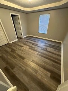 Empty bedroom with wood-look flooring, beige walls, white trim, and a window with blinds.