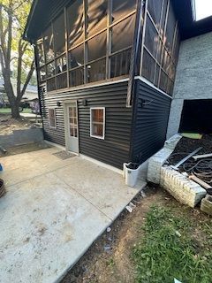 Black-sided building with a screened porch on top, a concrete patio, and a door.