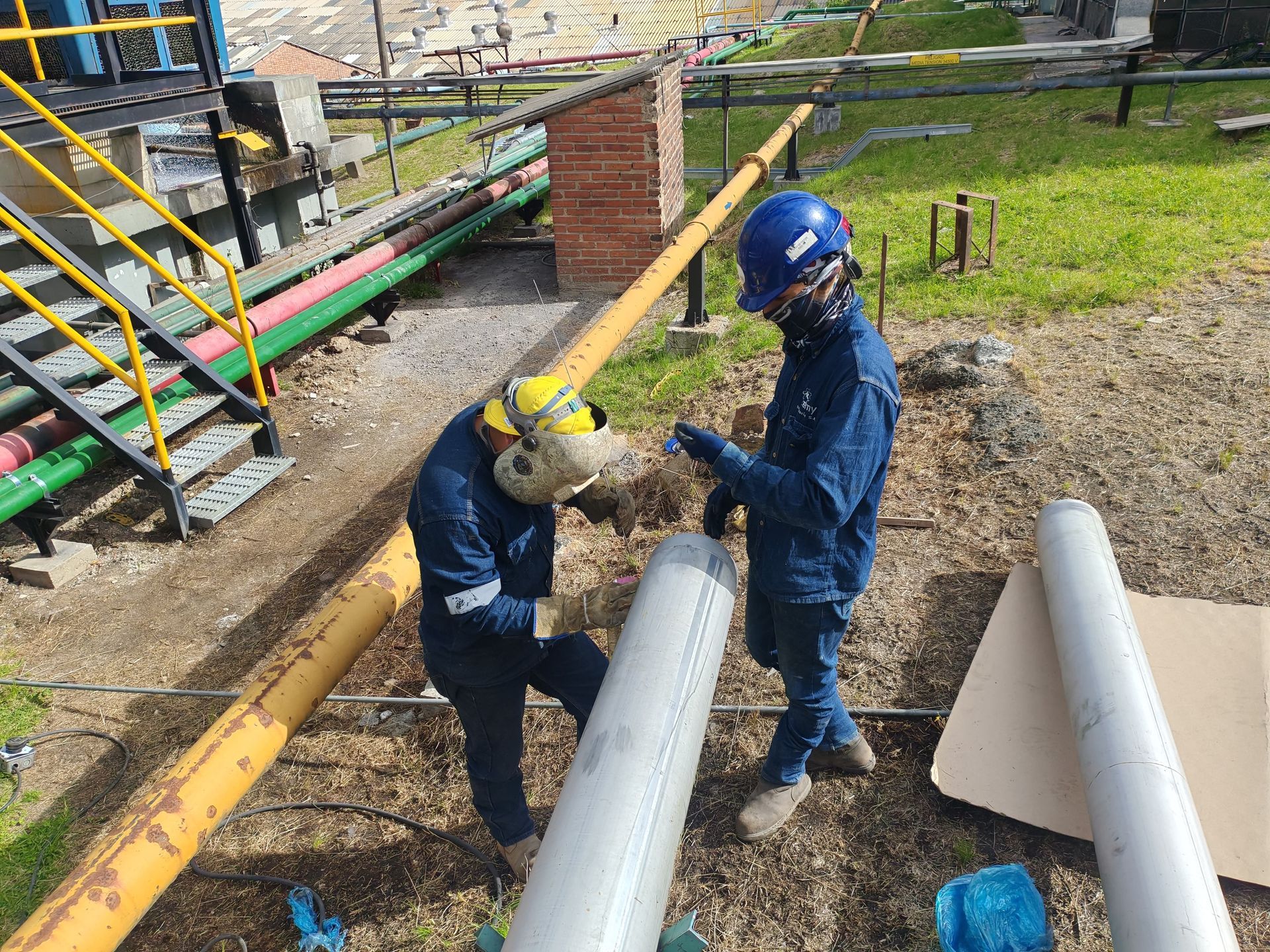 Dos trabajadores con trajes de seguridad azules inspeccionan grandes tuberías blancas