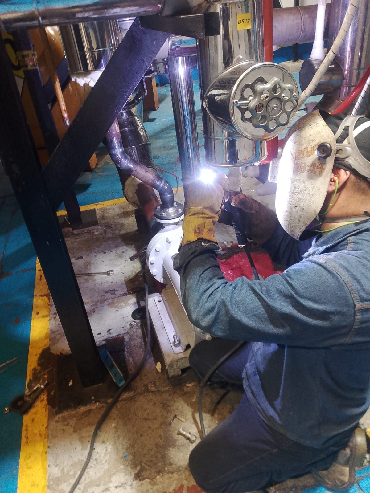 Un trabajador está soldando una estructura metálica en un taller, y lleva puesto un traje de protección y un casco.