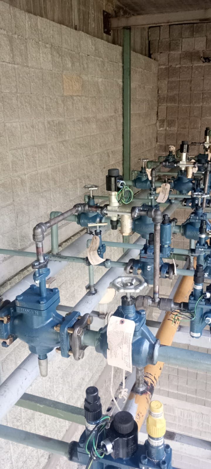 Montaje de bomba y tuberías industriales en un cuarto de servicio de hormigón, con válvulas y accesorios azules y blancos.