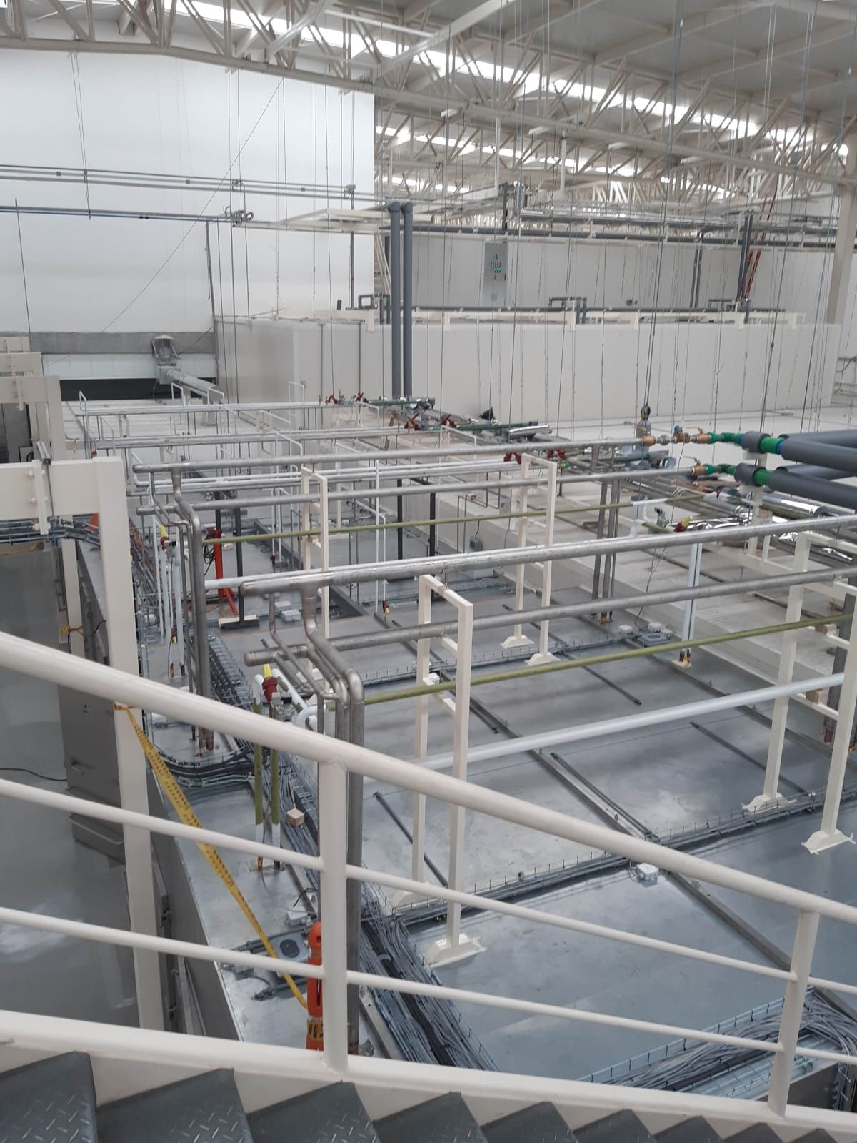 Instalación industrial con pasarelas y tuberías de metal blanco sobre una gran zona de tanques azules.