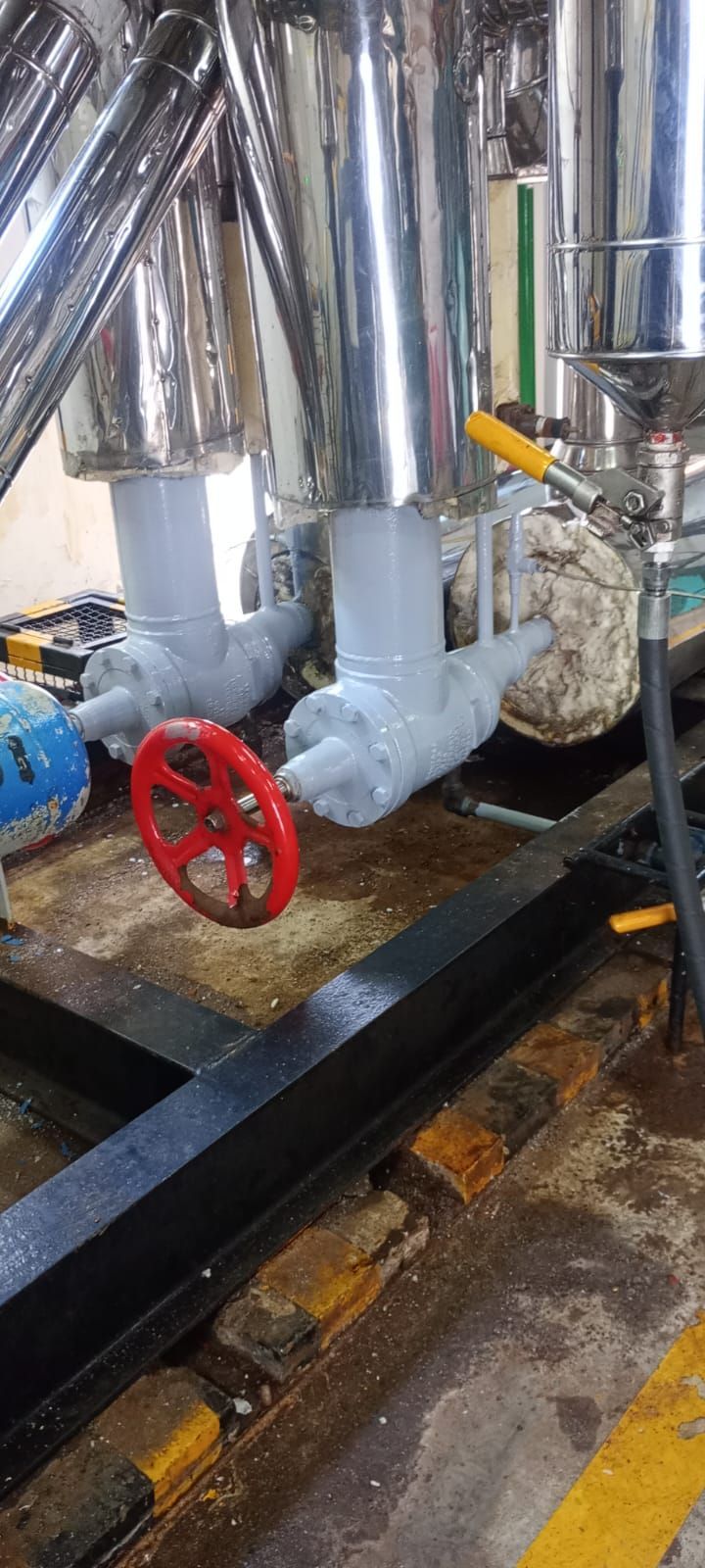Tubería industrial con rueda de válvula roja y tuberías aisladas en un entorno de sala de máquinas húmeda.