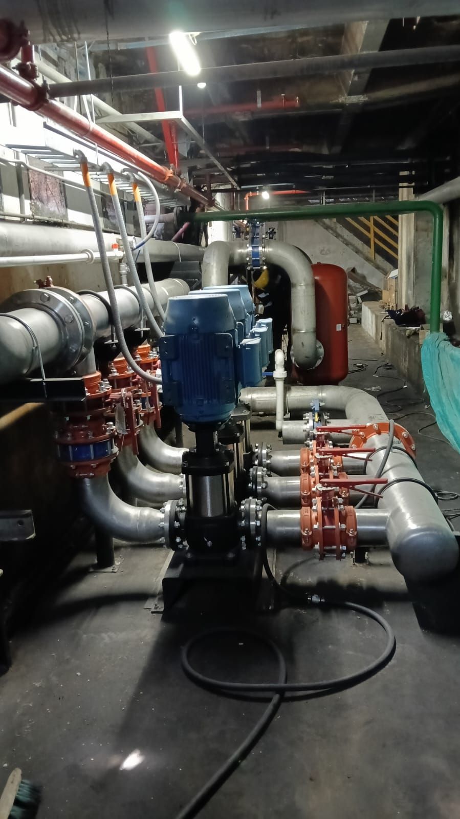 Maquinaria industrial y tuberías en una sala de máquinas, con bombas azules y rojas y grandes conductos plateados.