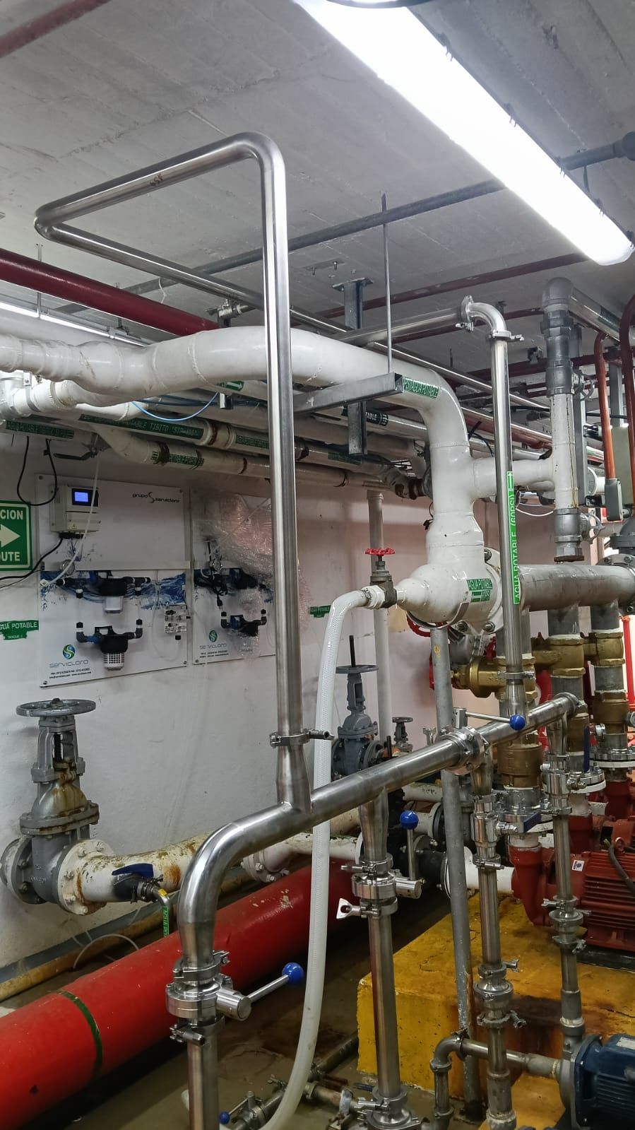 Tuberías y válvulas industriales en una sala de máquinas con tuberías rojas, blancas y amarillas en el techo.