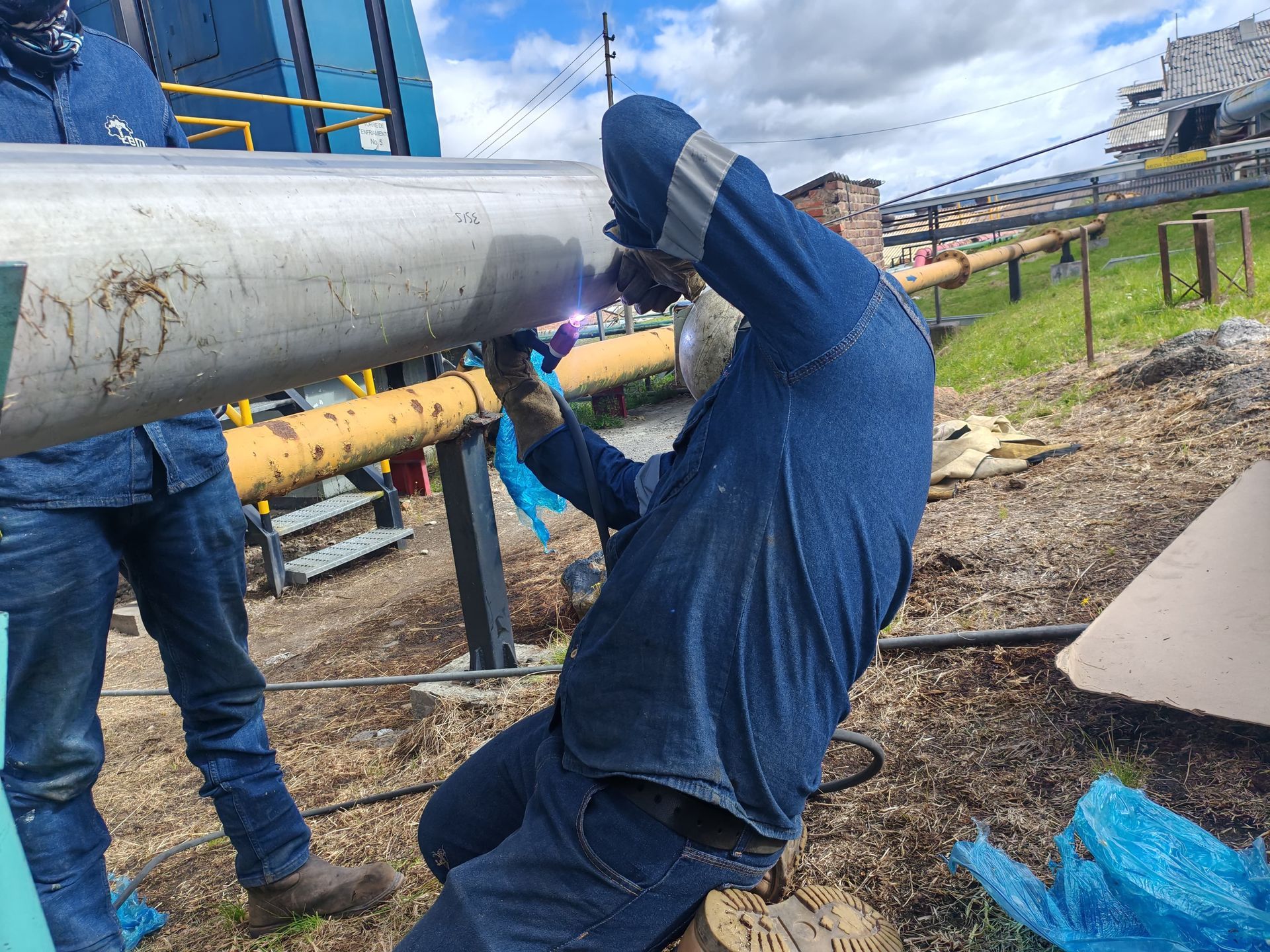 Trabajador con camisa azul manipulando una tubería grande en una obra de construcción al aire libre.