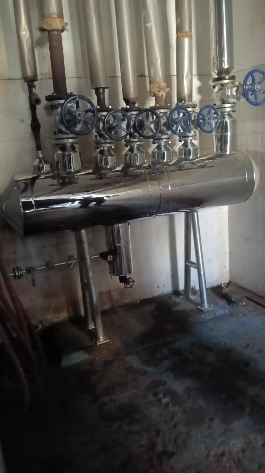Tuberías y válvulas industriales montadas sobre un gran tanque metálico horizontal en un cuarto de servicio.