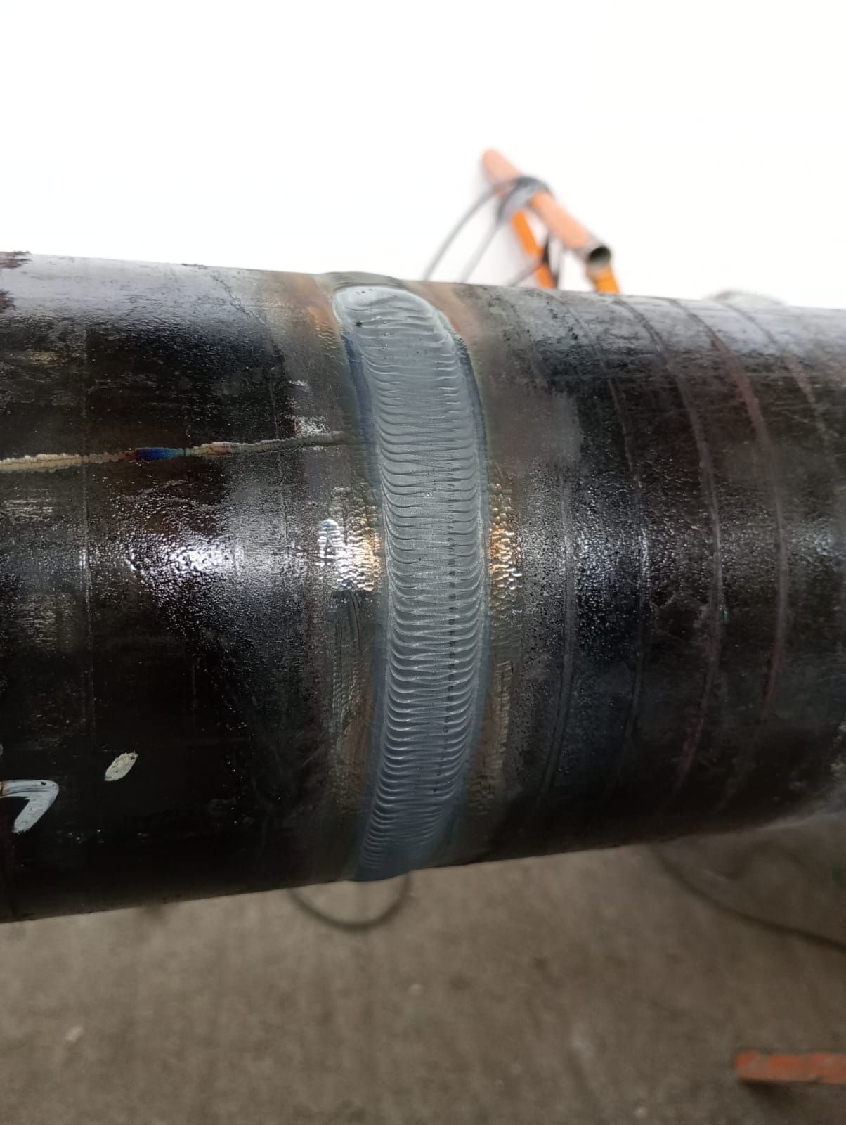 Primer plano de una tubería de metal negro con una costura soldada gris, con un trabajador borroso al fondo.