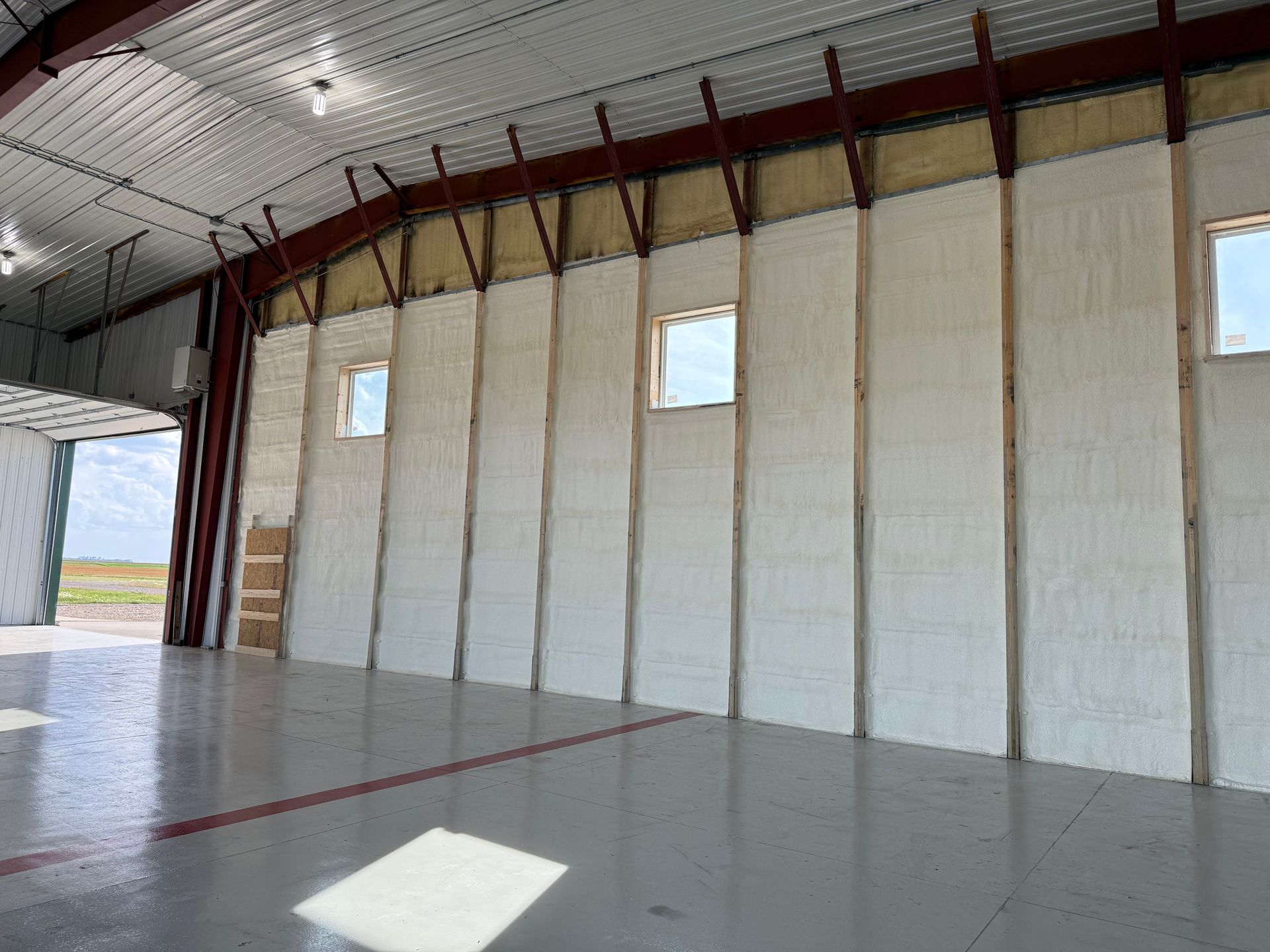 Interior of a large building with spray foam-insulated walls, wooden support beams, and a gray floor.
