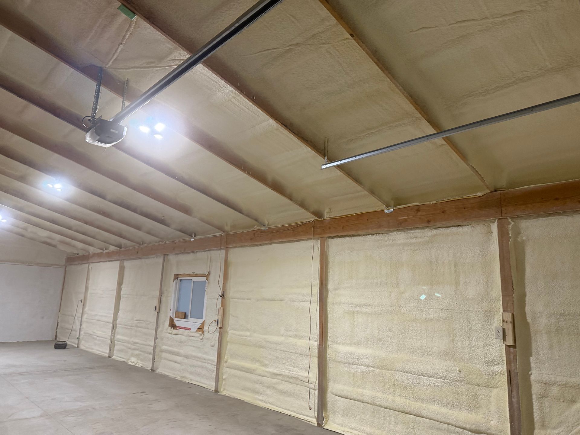 Interior of a garage or workshop with spray foam insulation on the walls and sloped ceiling, and a small window.