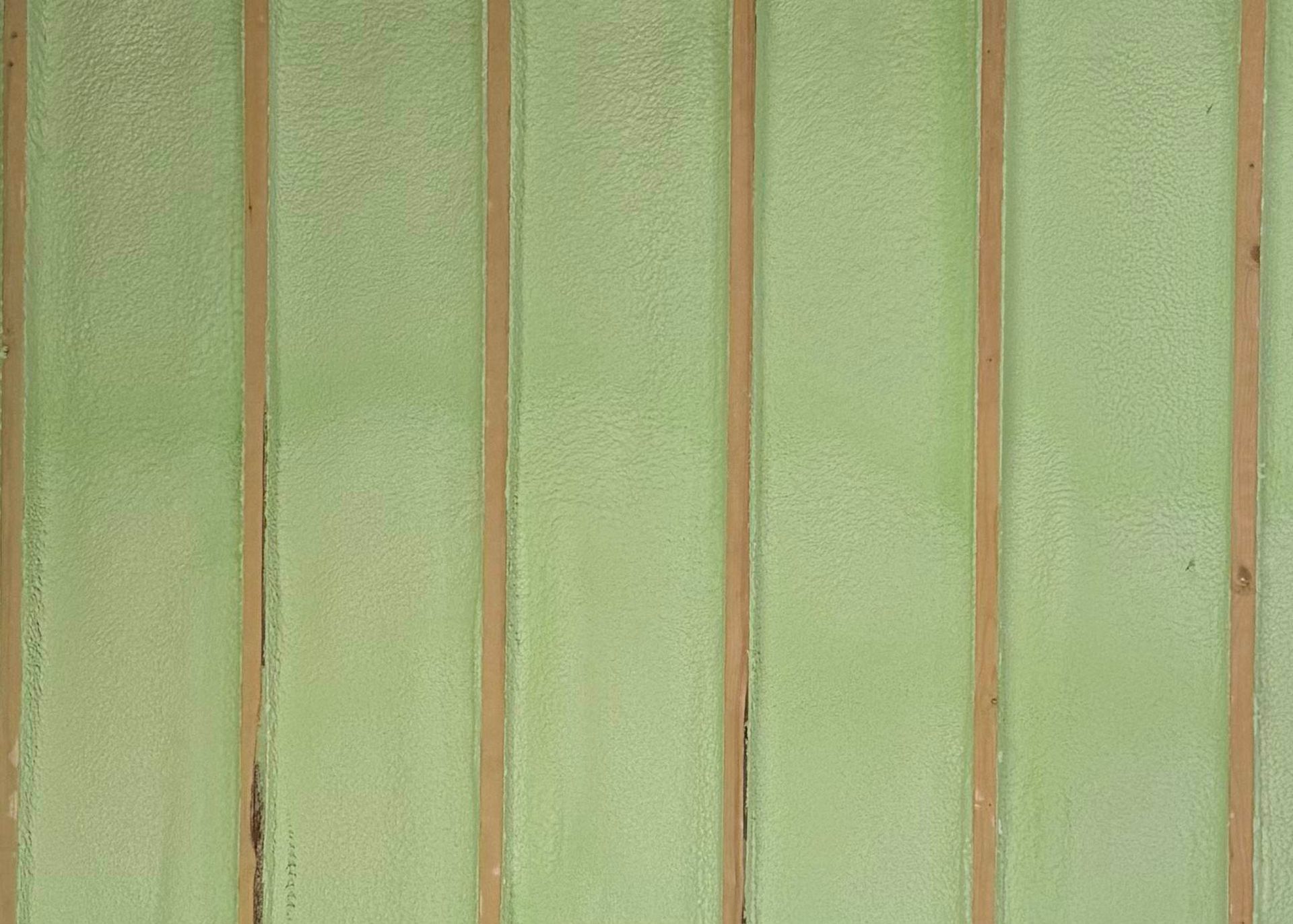 Pale green spray foam insulation applied between vertical wooden wall studs.