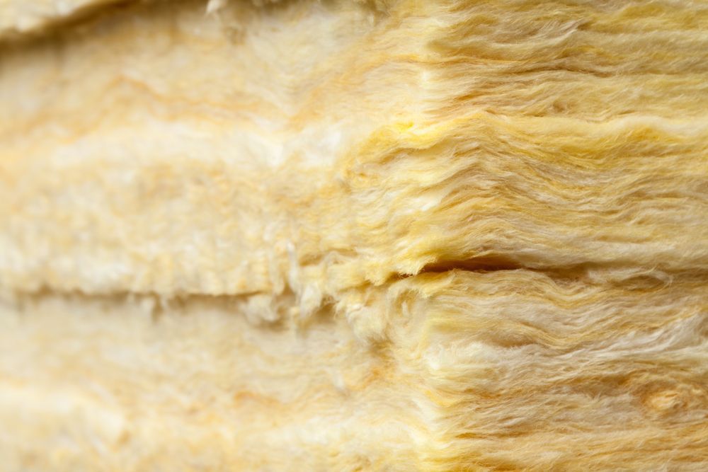 A close-up, angled view of stacked layers of yellow, fibrous fiberglass insulation material.