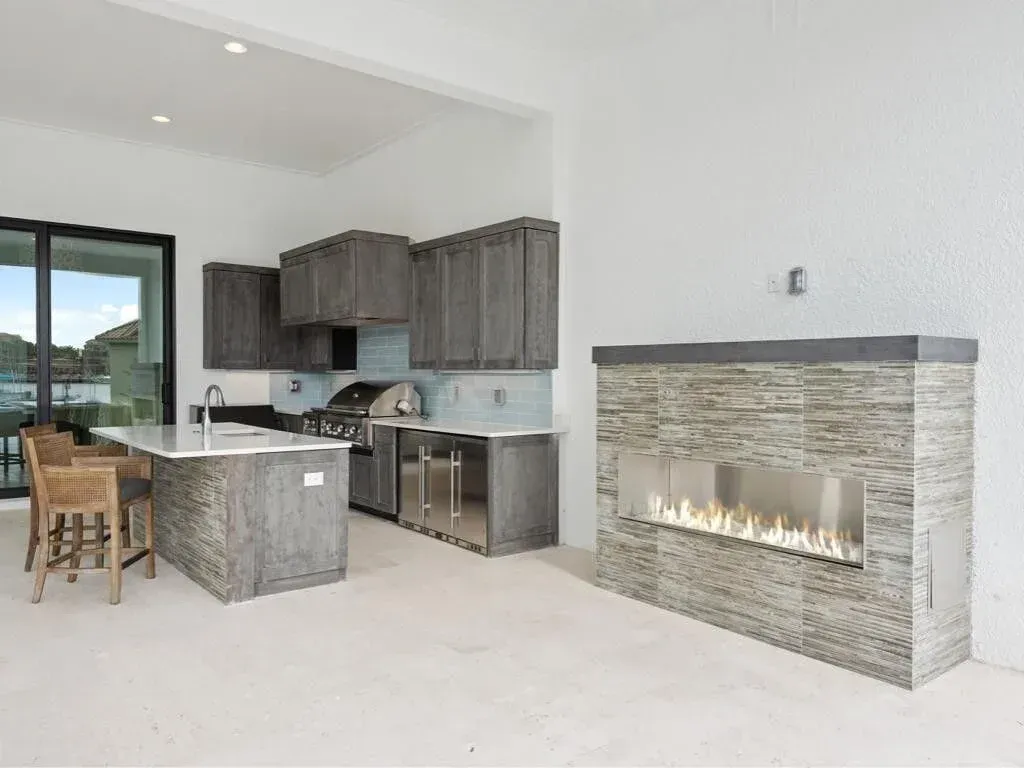 Bright open kitchen and living room with gray cabinets, island, and modern stone fireplace.
