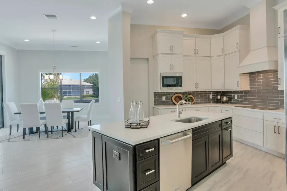 Bright modern kitchen with white cabinets, dark island, and open dining area with large windows