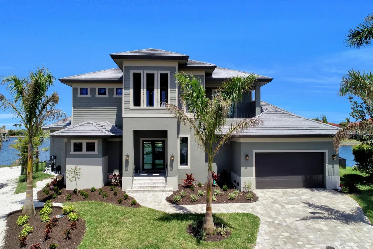 Modern two-story house with gray exterior, palm trees, and a two-car garage under a clear blue sky