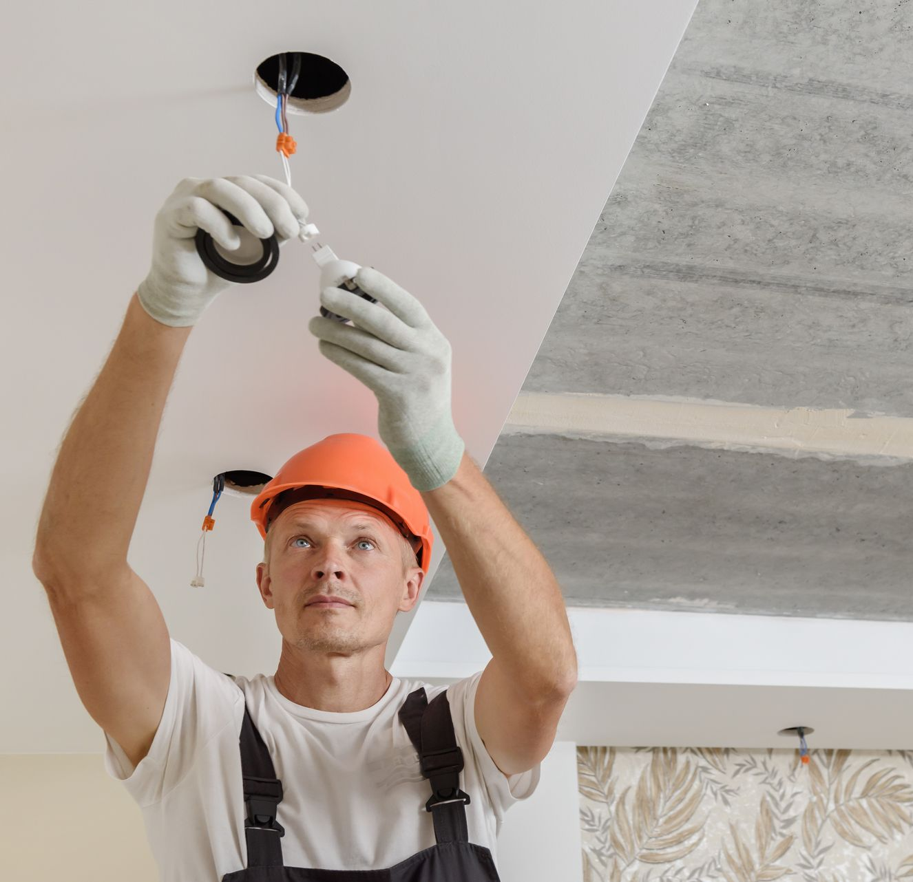 Worker installing a ceiling light fixture with tools and safety gear on a renovation site. Worker installing a ceiling light fixture with tools and safety gear on a renovation site.